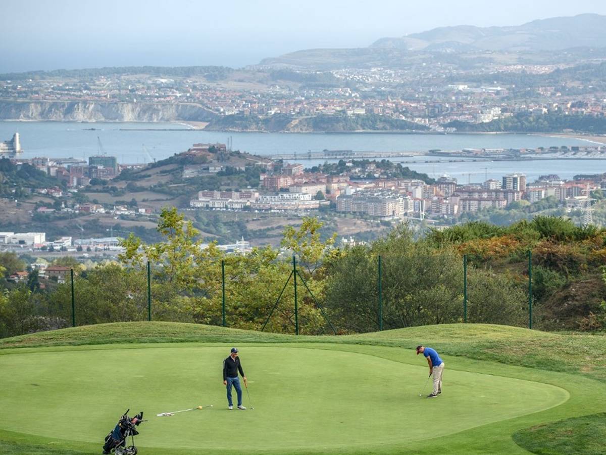 Two golfers putting out on the green at Meaztegi Golf, with the Bilbao coastline and Bay of Biscay in the distance